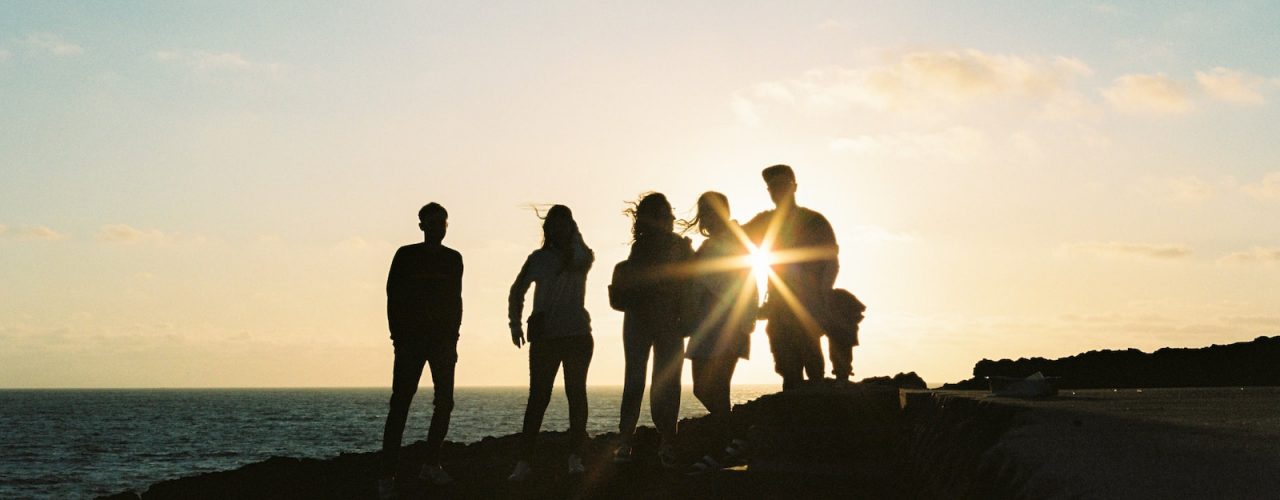 silhouette of people standing on rock formation near body of water during sunset