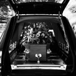 grayscale photo of hearse containing a coffin topped with flowers