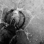 A boot splashes water on a textured surface